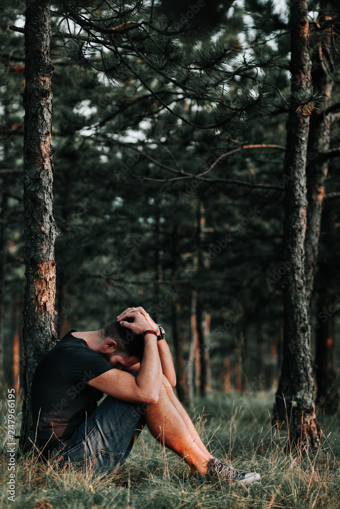 Young depressed man sitting alone in the forest