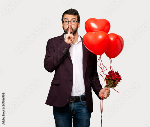 Man in valentine day showing a sign of silence gesture putting finger in mouth over isolated grey background © luismolinero