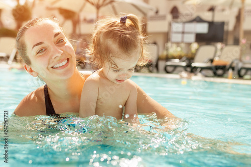 Mom and little daughter are played in the open swimming pool. Family with one child on vacation in warm countries. Positive people on vacation.