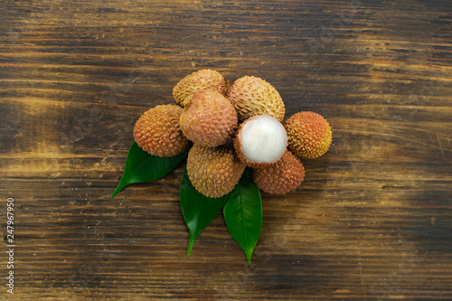 Fresh lychee and peeled showing the red skin and white flesh with green leaf on a wooden background. Lychi with leaves - tropical fruit. photo