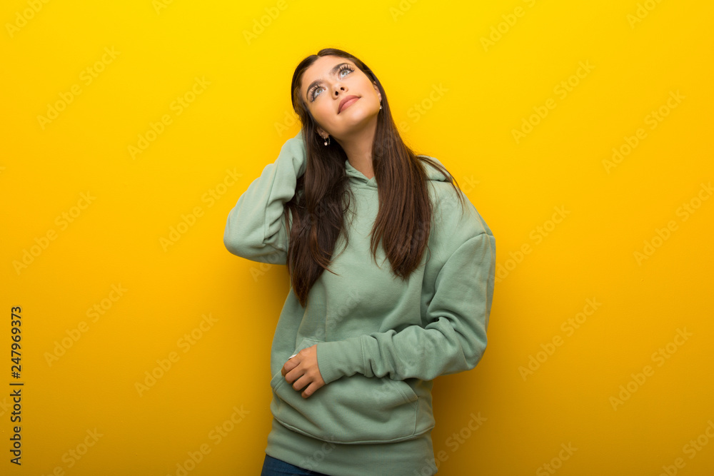 Teenager girl with green sweatshirt on yellow background thinking an idea while scratching head Teenager girl with green sweatshirt on yellow background thinking an idea while scratching head