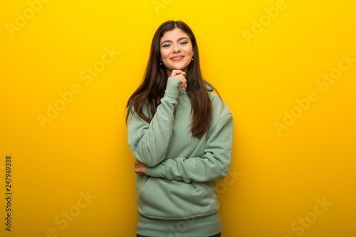 Teenager girl with green sweatshirt on yellow background smiling and looking to the front with confident face © luismolinero