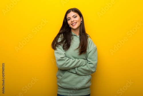 Teenager girl with green sweatshirt on yellow background looking up while smiling © luismolinero