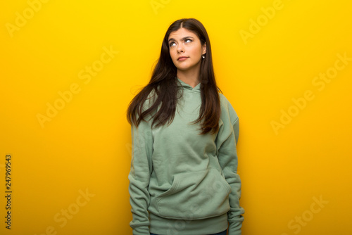 Teenager girl with green sweatshirt on yellow background looking up with serious face © luismolinero