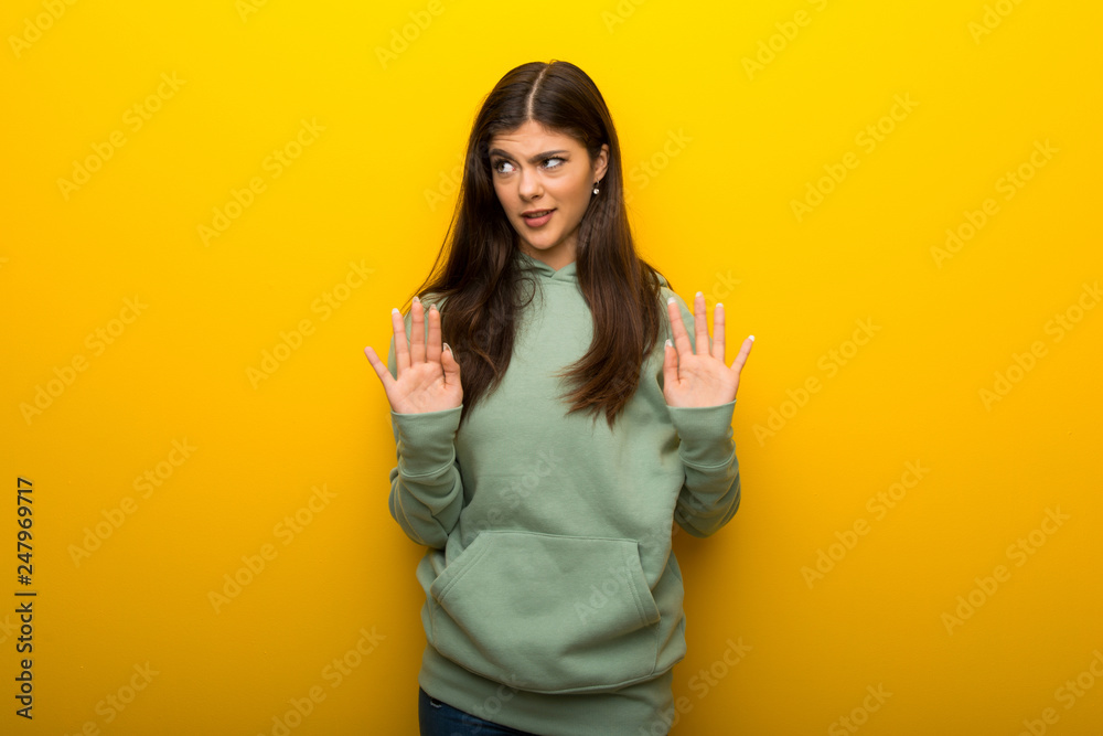 Teenager girl with green sweatshirt on yellow background making stop gesture with both hands