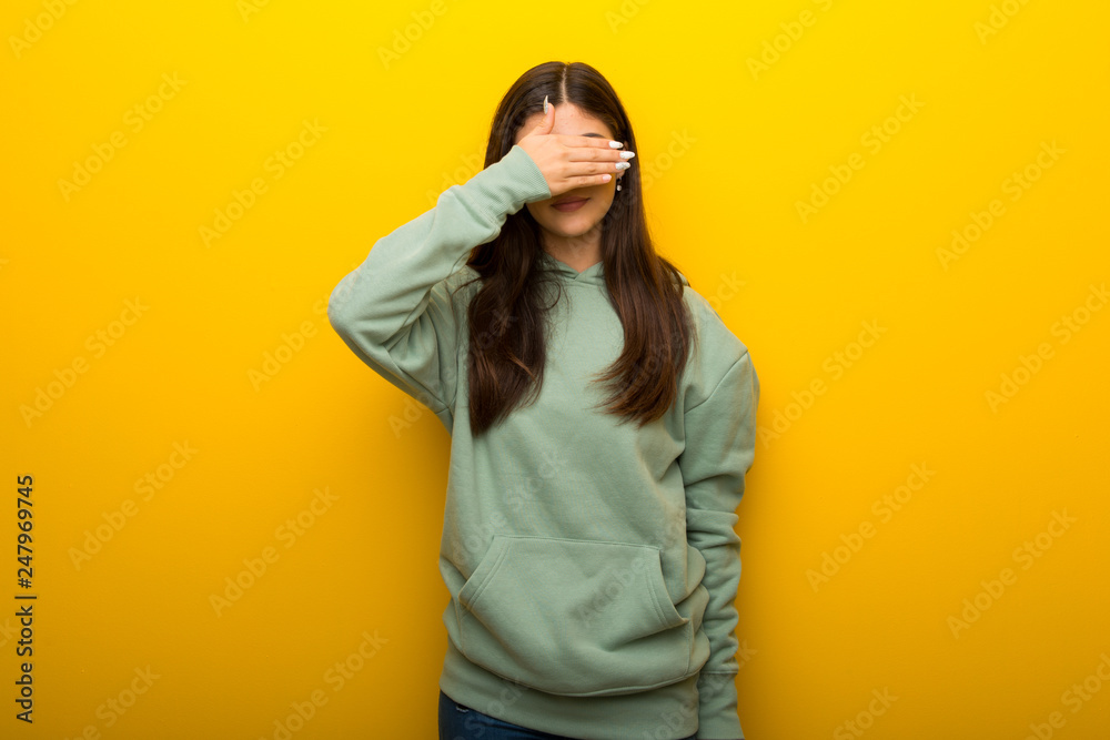 Teenager girl with green sweatshirt on yellow background covering eyes by hands. Do not want to see something Teenager girl with green sweatshirt on yellow background covering eyes by hands. Do not want to see something