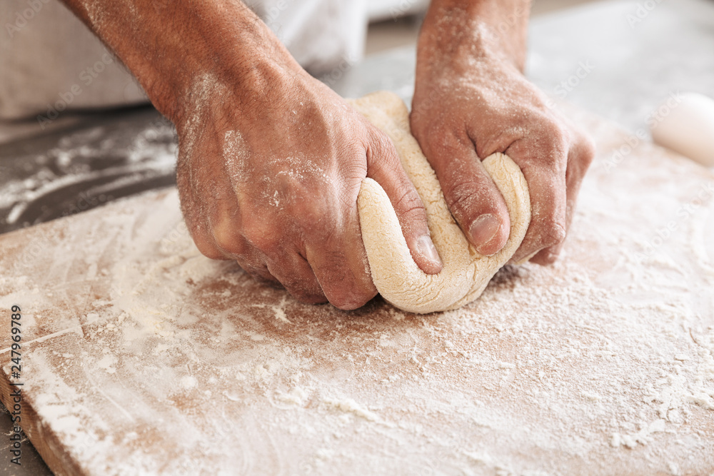 Closeup portrait of handsome male hands making dough for bread, on table at bakery or kitchen