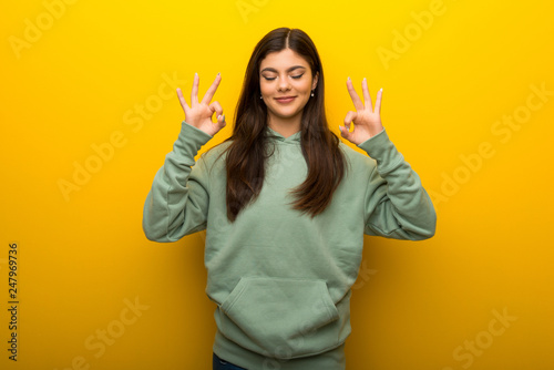 Teenager girl with green sweatshirt on yellow background in zen pose