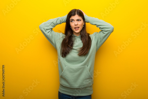 Teenager girl with green sweatshirt on yellow background takes hands on head because has migraine © luismolinero