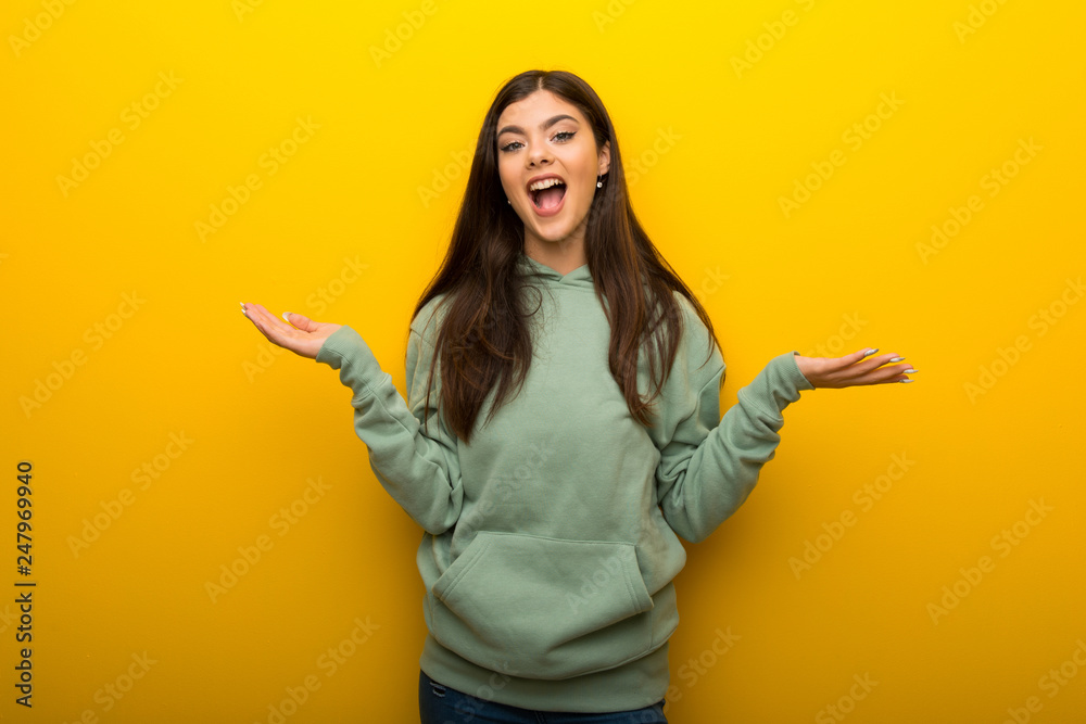 Teenager girl with green sweatshirt on yellow background with surprise and shocked facial expression Teenager girl with green sweatshirt on yellow background with surprise and shocked facial expression