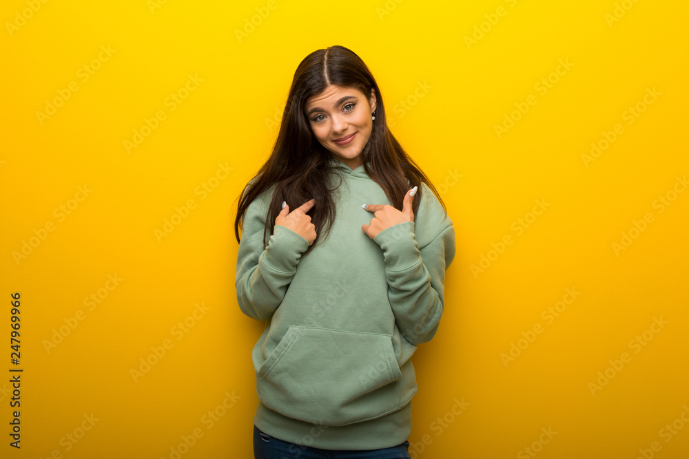 Teenager girl with green sweatshirt on yellow background with surprise facial expression