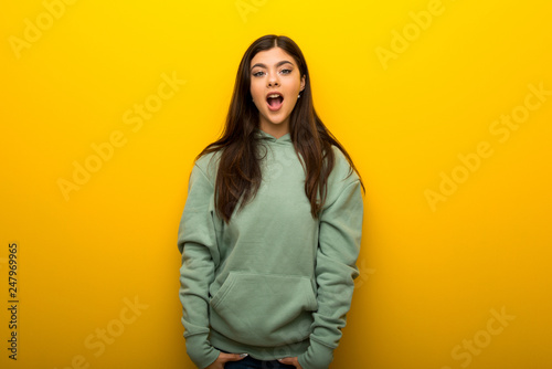Teenager girl with green sweatshirt on yellow background with surprise and shocked facial expression