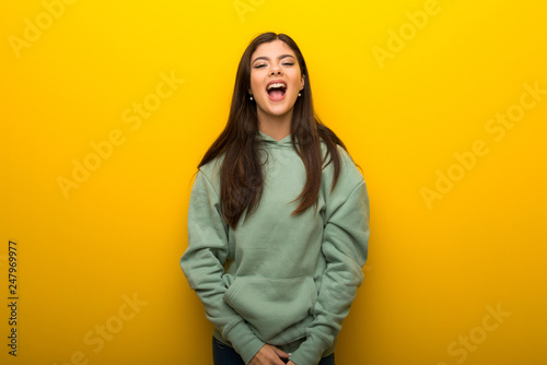 Teenager girl with green sweatshirt on yellow background shouting to the front with mouth wide open © luismolinero