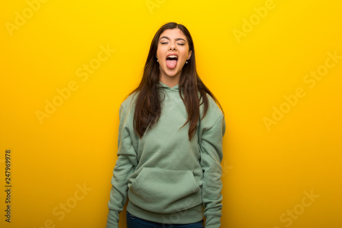 Teenager girl with green sweatshirt on yellow background showing tongue at the camera having funny look © luismolinero