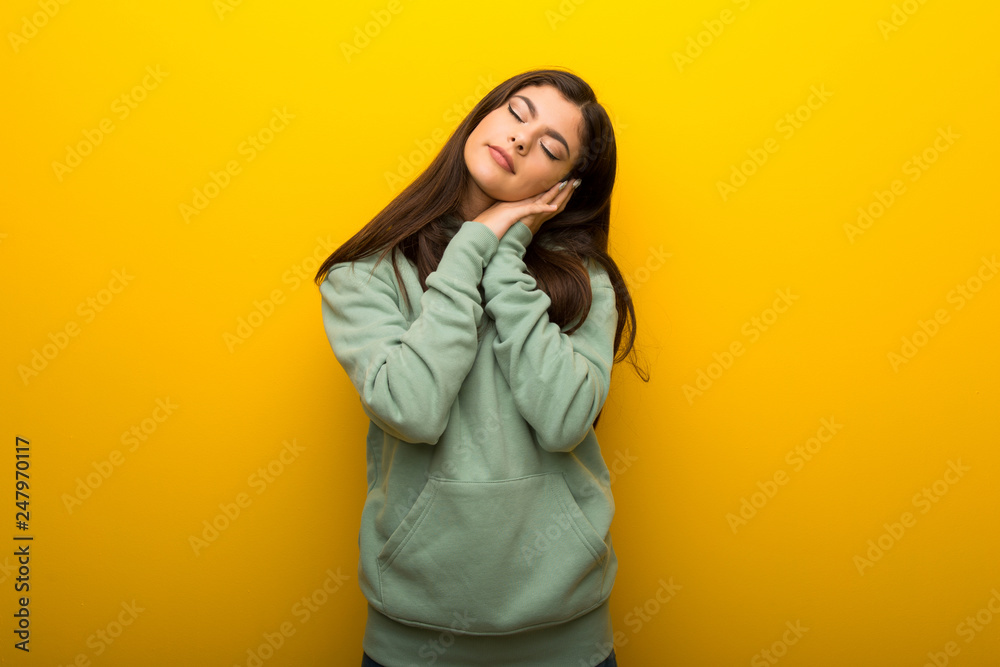 Teenager girl with green sweatshirt on yellow background making sleep gesture in dorable expression