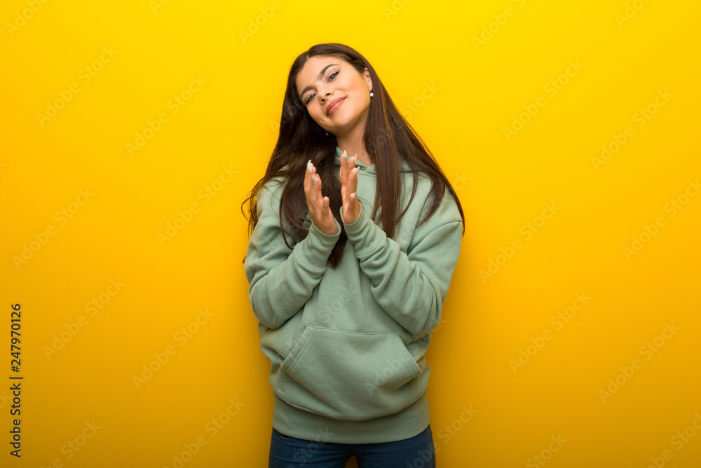 Teenager girl with green sweatshirt on yellow background applauding after presentation in a conference Teenager girl with green sweatshirt on yellow background applauding after presentation in a conference