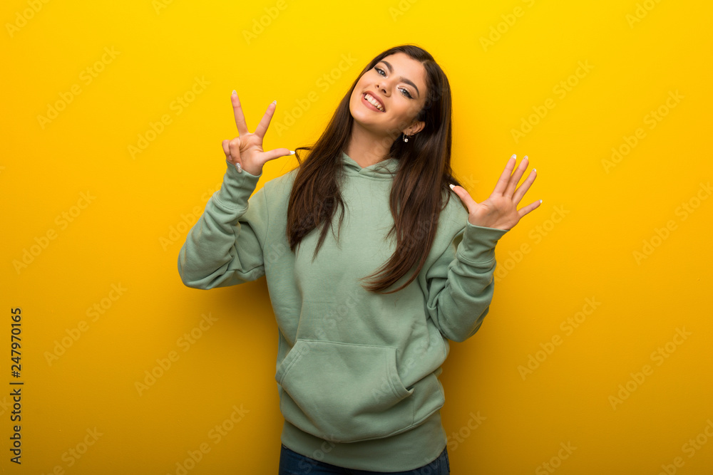 Teenager girl with green sweatshirt on yellow background counting eight with fingers Teenager girl with green sweatshirt on yellow background counting eight with fingers