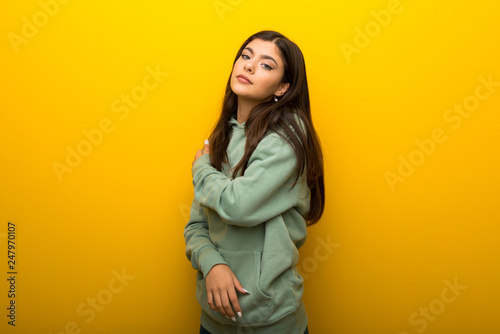 Teenager girl with green sweatshirt on yellow background suffering from pain in shoulder for having made an effort © luismolinero