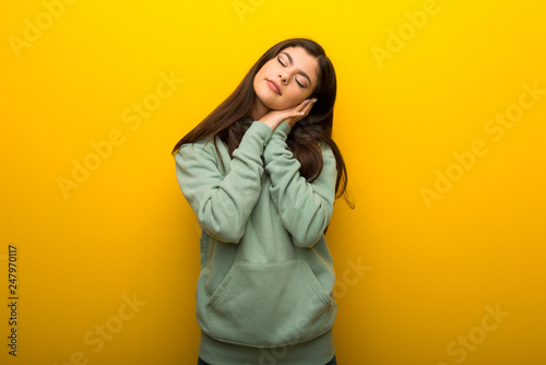 Teenager girl with green sweatshirt on yellow background making sleep gesture in dorable expression © luismolinero