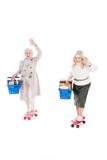 happy senior women riding penny boards and holding shopping baskets isolated on white