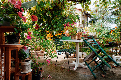 Sunny terrace with flowers  table and green chairs