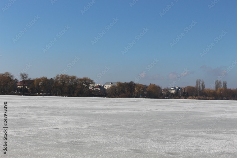  The lake is covered with ice. In the distance you can see the shore with trees