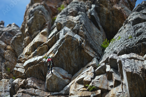 The climber climbs up the rope against the background of a huge rock wall. Tilt-Shift effect.