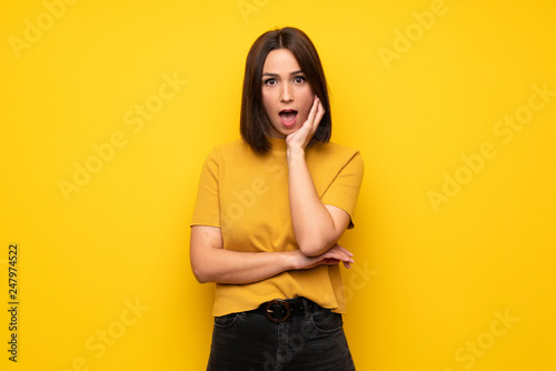Young woman over yellow wall surprised and shocked while looking right