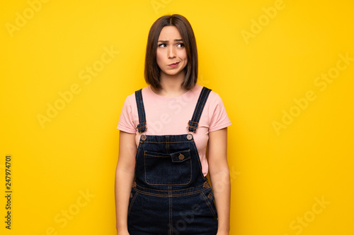 Young woman over yellow wall feeling upset