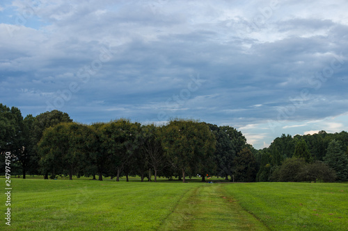 Park with a smooth green lawn, beautiful trees and picturesque clouds. Beautiful clouds in the sky over the summer forest. Landscaping. Park Milliken Arboretum, Spartanburg, South Carolina, USA
