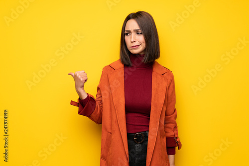 Young woman with coat unhappy and pointing to the side © luismolinero