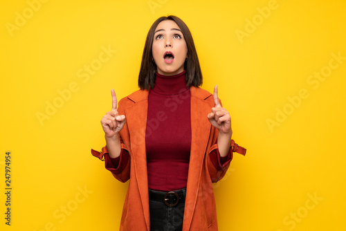 Young woman with coat surprised and pointing up