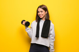 Young sport woman over yellow background making weightlifting