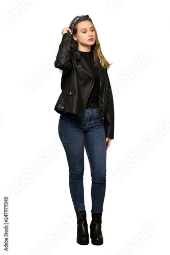 A full-length shot of a Teenager girl with leather jacket having doubts while scratching head on isolated white background