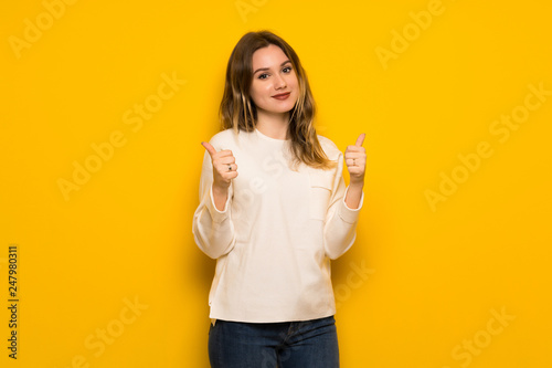 Teenager girl over yellow wall giving a thumbs up gesture with both hands and smiling