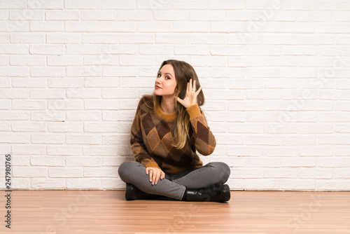 Teenager girl sitting on the floor listening to something by putting hand on the ear