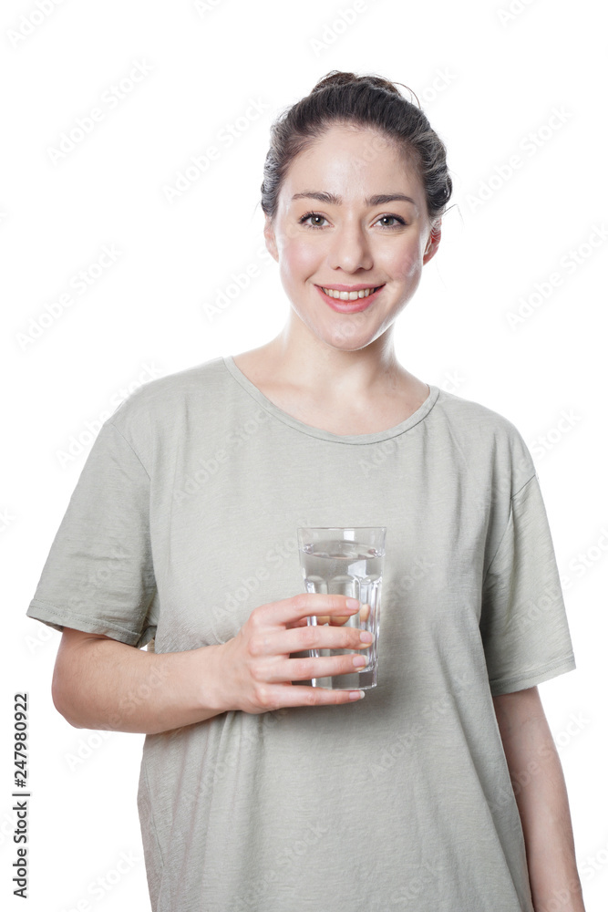 cheerful young woman in her 20s with natural make-up and brunette hair bun holding glass of faucet water - isolated on white background cheerful young woman in her 20s with natural make-up and brunette hair bun holding glass of faucet water - isolated on white background