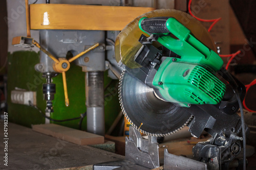 The green electrical circular mitre saw on the carpenter workbench in the workroom. Soft focus