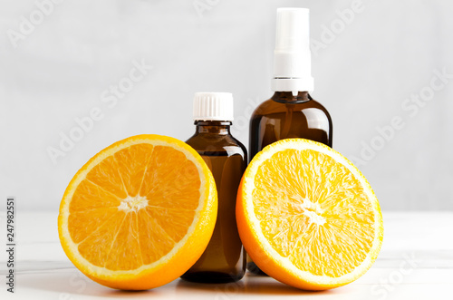 Juicy oranges and bottles with aromatic oils for aroma therapy standing on white table against wall