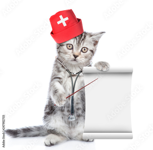 Kitten with stethoscope on his neck and with medical hat pointing on empty list. isolated on white background