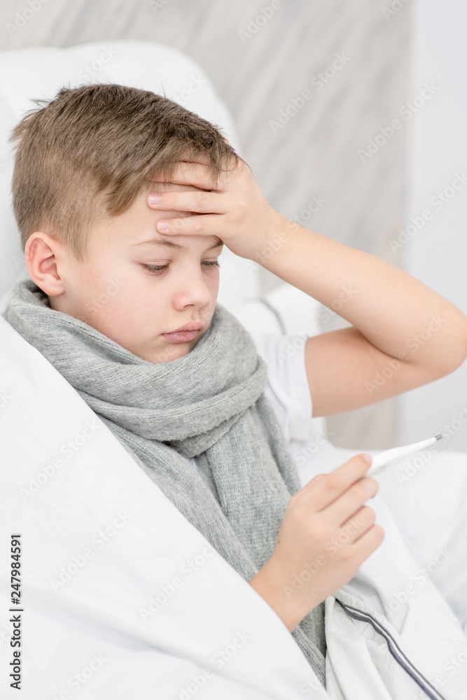 Sick boy on the bed checks the temperature with a thermometer Sick boy on the bed checks the temperature with a thermometer