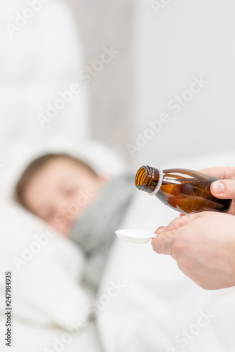 Sick little boy awaits his medication pouring in a spoon in the foreground
