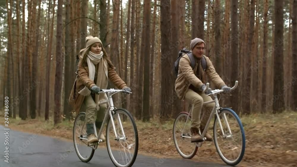 Young happy couple with backpacks riding bicycles on wet asphalt road in the park on autumn day Young happy couple with backpacks riding bicycles on wet asphalt road in the park on autumn day