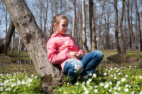 cute girl child brunette in a pink jacket in spring in the park with the first spring flowers on the lawn