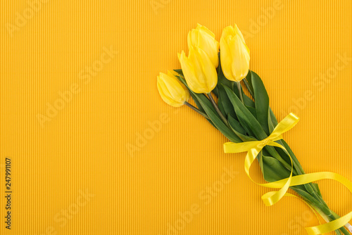 top view of yellow tulip bouquet with ribbon on orange background for international women's day