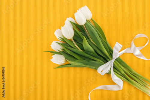 top view of white tulip bouquet with ribbon on orange background