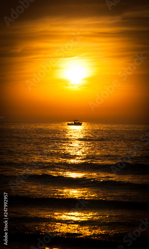 Silhouette of the fisherman or leisure boat sailing toward golden sunset with saturated sky and clouds. Beautiful seascape in the evening. Harmony with nature idea. Tranquility and freedom background. © Elena Dijour