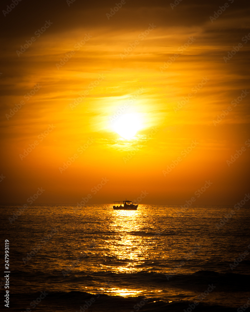 Silhouette of the fisherman or leisure boat sailing toward golden sunset with saturated sky and clouds. Beautiful seascape in the evening. Harmony with nature idea. Tranquility and freedom background.