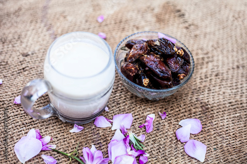 Close up shot of popular Indian & Asian Khajor dudh or dates milk in a transparent glass bowl along with raw dates on a brown colored surface or background. photo