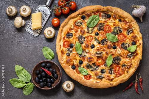 pizza with tomatoes, cheese, mushrooms, olives and spinach on a dark background